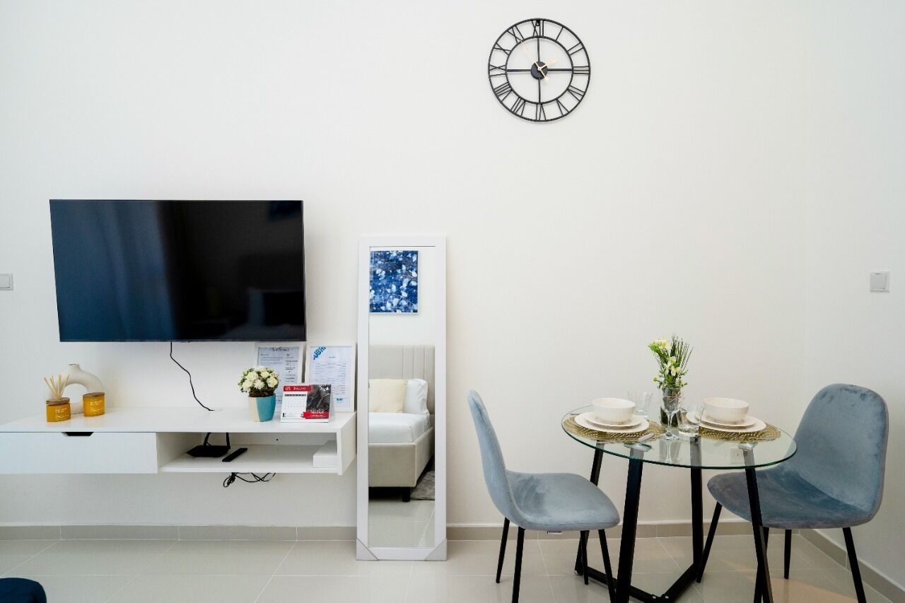 A modern living room with a flat-screen TV, a wall clock, a sofa, a coffee table, and two chairs.