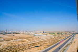 An aerial view of a desert landscape with a highway, buildings, and a city skyline in the distance. - Tanin - Studios at Damac Hills Carson Tower C (Dubai)