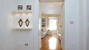 A hallway with white walls, wooden flooring, and decorative wall art. There are doors on the right and a window at the end of the hallway. - Palestrina   Prati area, Rome (ROMA)