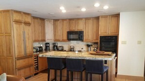 A modern kitchen with wooden cabinets, a central island with bar stools, a microwave, and a coffee maker.