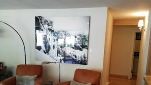 A living room with two brown leather armchairs, a white ottoman, and a floor lamp. A large black and white photograph is on the wall.