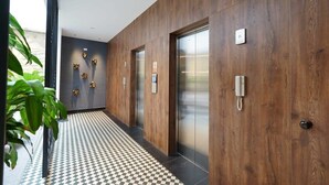 Een moderne hal met houten lambrisering, twee liften en een geruit vloerpatroon.