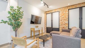 Een moderne woonkamer met een stenen accentmuur, een flatscreen televisie, een grijze bank, een houten stoel en een kleine tafel.