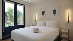 Hotelkamer met een groot bed, twee ingelijste foto's aan de muur, een nachtkastje met een lamp en uitzicht door een raam met balkon.