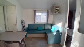 Ein Zimmer mit einem blauen Sofa, einem Esstisch mit Stühlen, einem Fenster mit gemusterten Vorhängen und einem weißen Heizkörper.