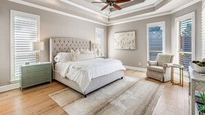 A bedroom with a large bed, a ceiling fan, and a view of the outdoors through the windows. - Luxurious Home-Resort Style Pool & Game Room (Plano)