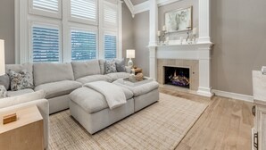 A modern living room with a sectional sofa, fireplace, and large windows with blinds. - Luxurious Home-Resort Style Pool & Game Room (Plano)