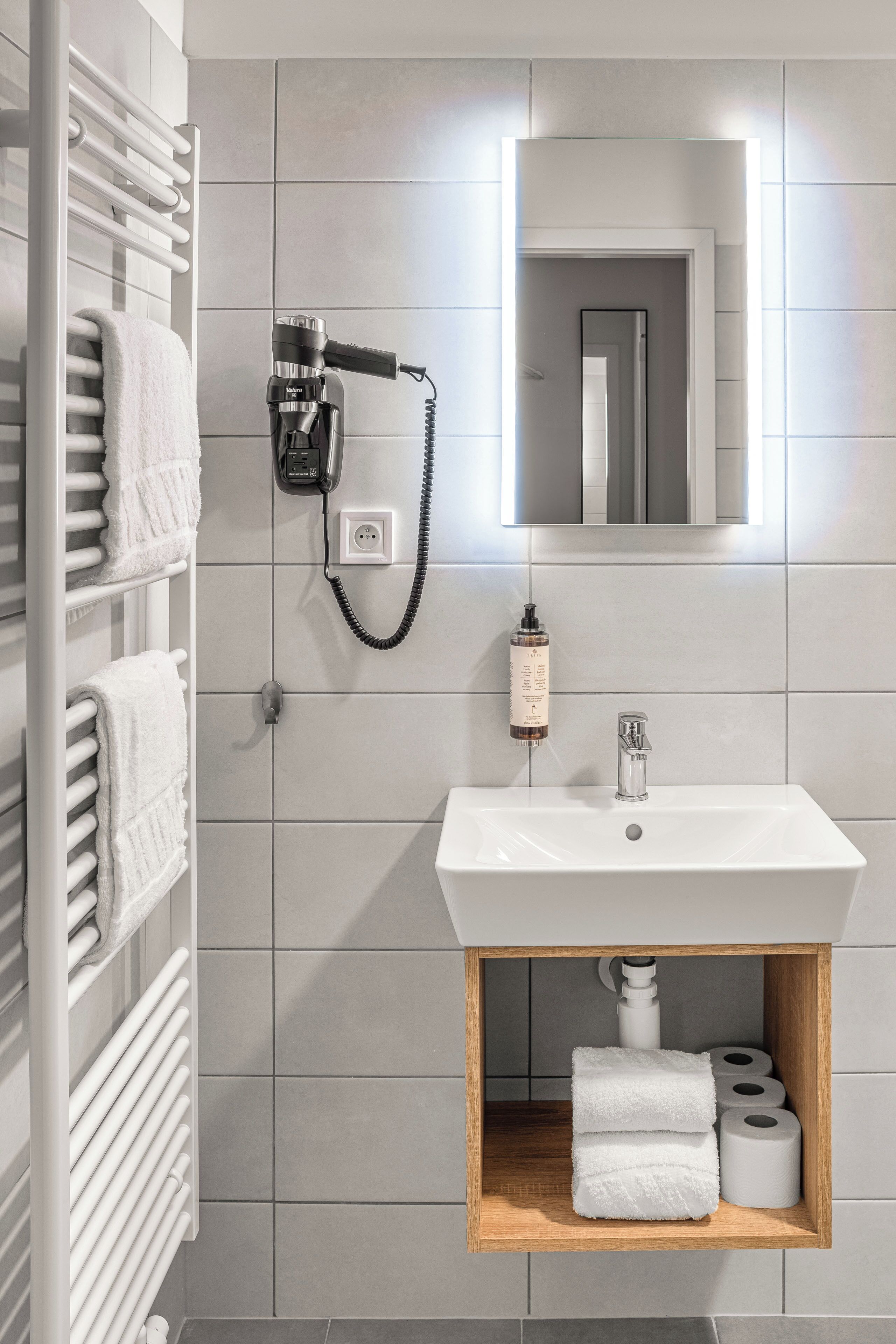 Een moderne badkamer met een wit wastafelmeubel, een spiegel, een handdoekrek en een plank met handdoeken en toiletpapier.