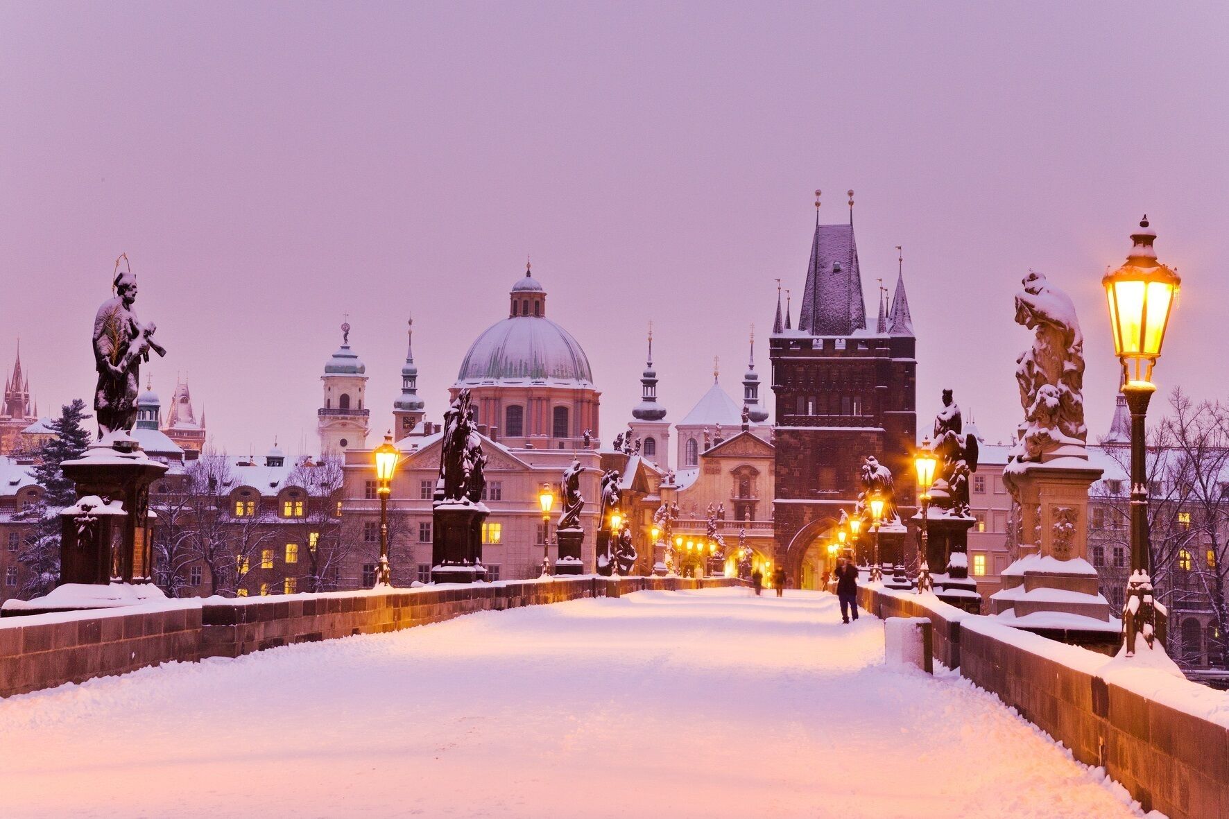 A snow-covered plaza with statues and a historic building in the background.