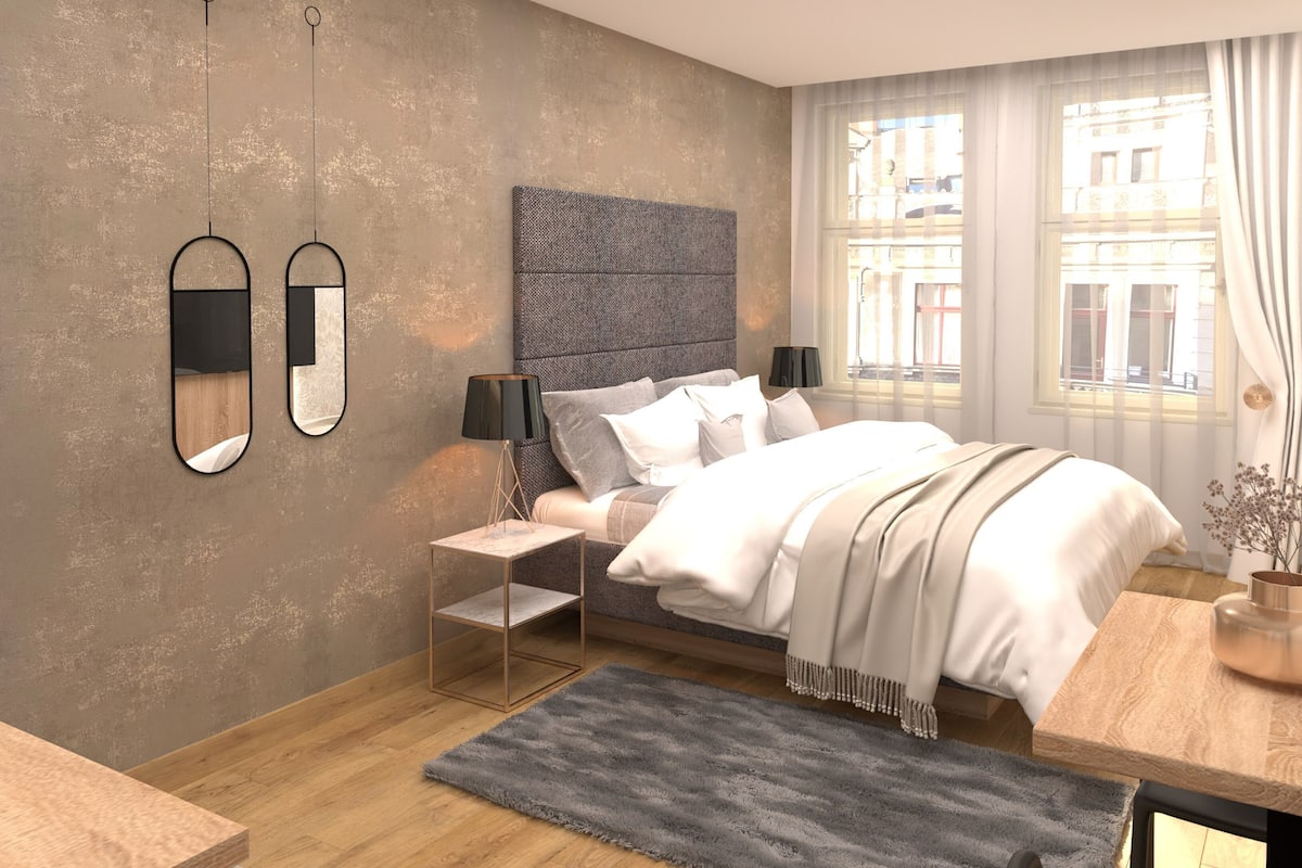 A modern bedroom with a bed, bedside tables, a rug, and a view of the city through large windows.