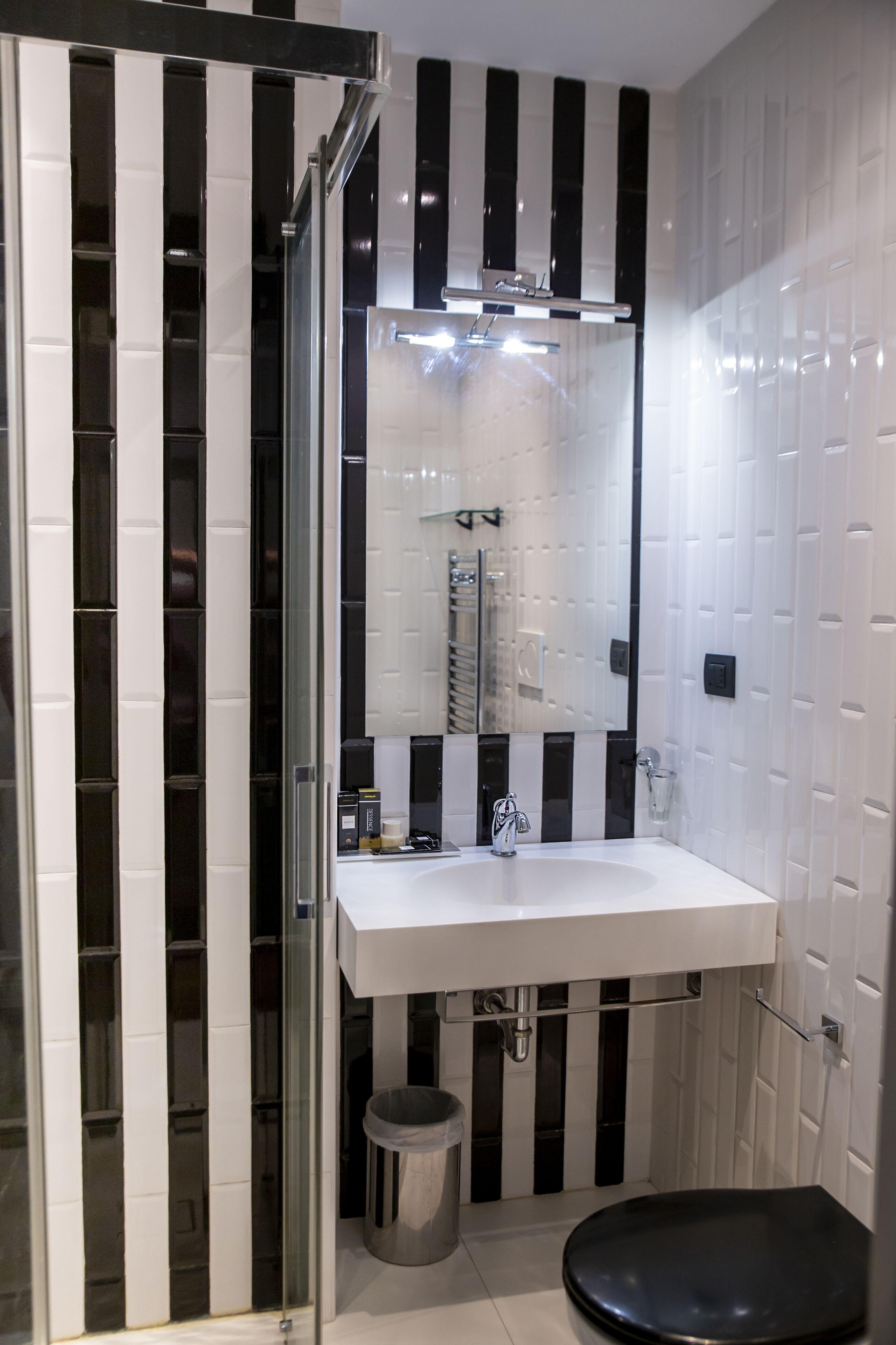 A modern bathroom with a white sink, black and white striped walls, a glass shower enclosure, and a black toilet.