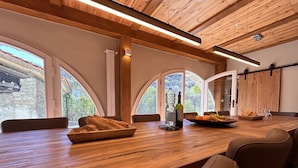 Une table de salle à manger en bois, avec du pain, une bouteille et des fruits au centre, entourée de chaises en cuir.