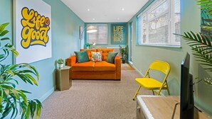 Una sala de estar con paredes azul verdosas, un sofá, un sillón amarillo y un televisor.