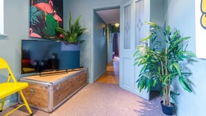 Un pasillo con un baúl antiguo, un televisor y plantas en macetas.