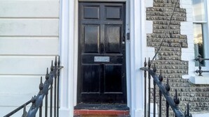 Una puerta negra con una placa, revestimiento blanco y una pared de piedra decorativa.