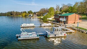 Une jetée au bord du lac avec plusieurs bateaux, un bâtiment en bois doté d’un toit vert et une zone herbeuse avec des arbres.