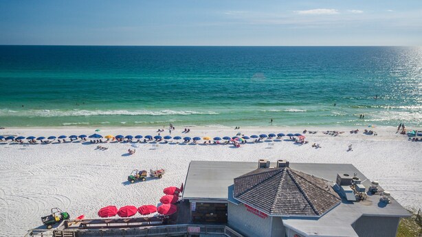 A beach with umbrellas and a building with a sign that reads "MIRACLE THE RESTAURANT". - LF120 Between the Gulf and Lake Stewart, you are steps to the pool and beach! (Miramar Beach)