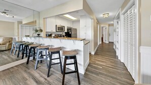 A modern kitchen with white cabinets, a central island with bar stools, and a dining area with a sofa and coffee table. - LF120 Between the Gulf and Lake Stewart, you are steps to the pool and beach! (Miramar Beach)