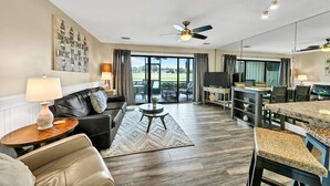 A spacious living room with a black leather sofa, a round coffee table, and a dining area with a marble table and chairs. - LF120 Between the Gulf and Lake Stewart, you are steps to the pool and beach! (Miramar Beach)