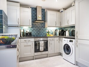 Une cuisine compacte avec des meubles blancs, un four encastré, un lave-linge et un crédence recouverte de carreaux bleus.