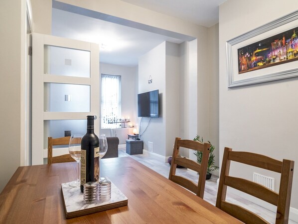 Un coin repas avec une table en bois, des chaises, une bouteille de vin et un tableau encadré au mur.