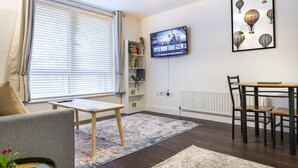Un salon moderne comprenant un canapé, une table basse, un téléviseur fixé au mur, une table à manger avec des chaises et une bibliothèque.