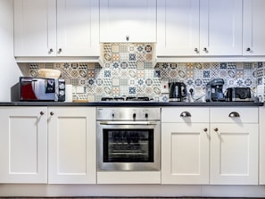 Une cuisine moderne avec des meubles blancs, un four encastré, une cuisinière et un dosseret carrelé.