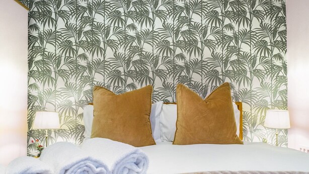 Un lit bien fait, avec des serviettes blanches pliées en rouleau, deux oreillers marron et une couvre-lit à motifs.