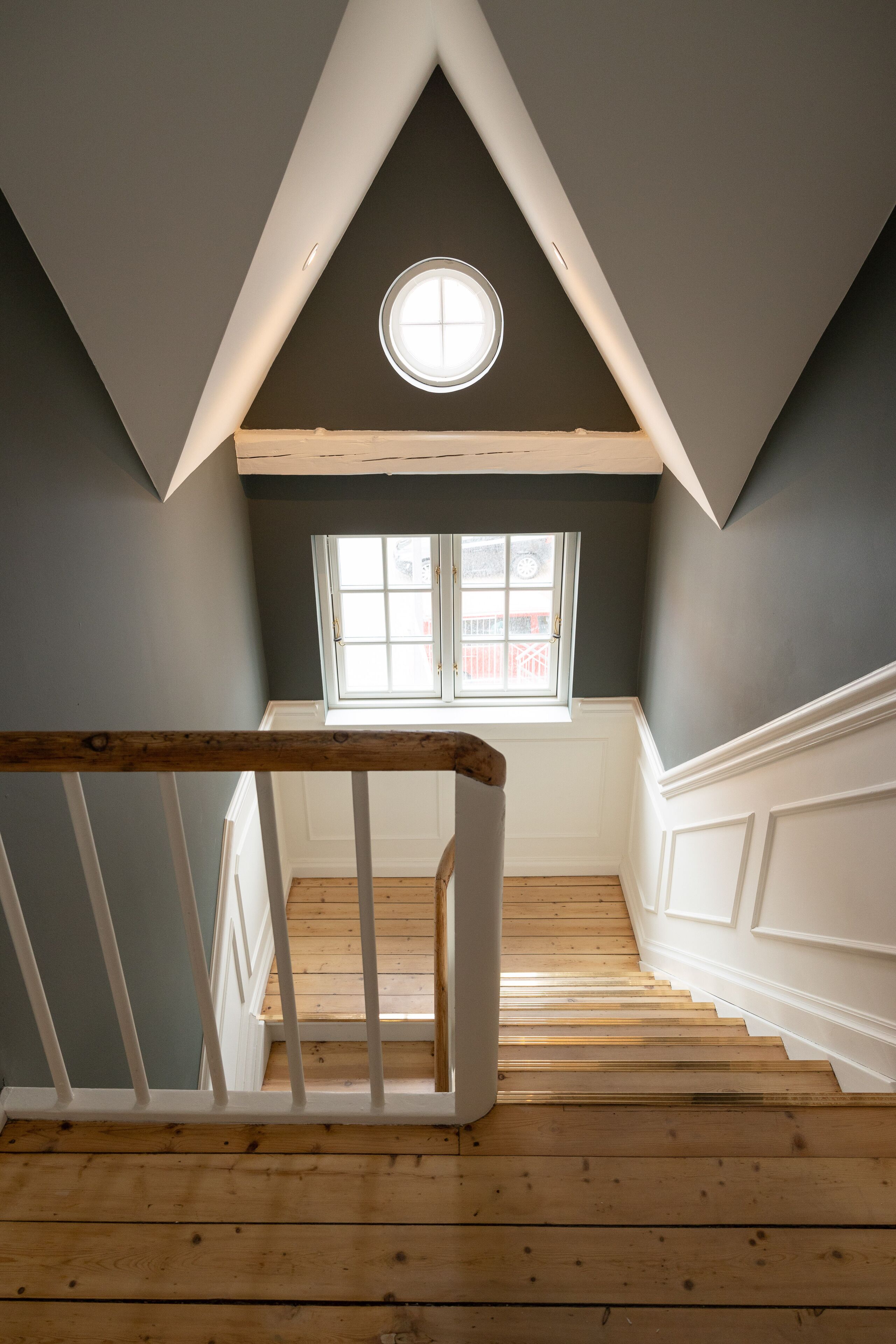 A staircase with wooden steps and white railings, leading to a room with a skylight and a window.