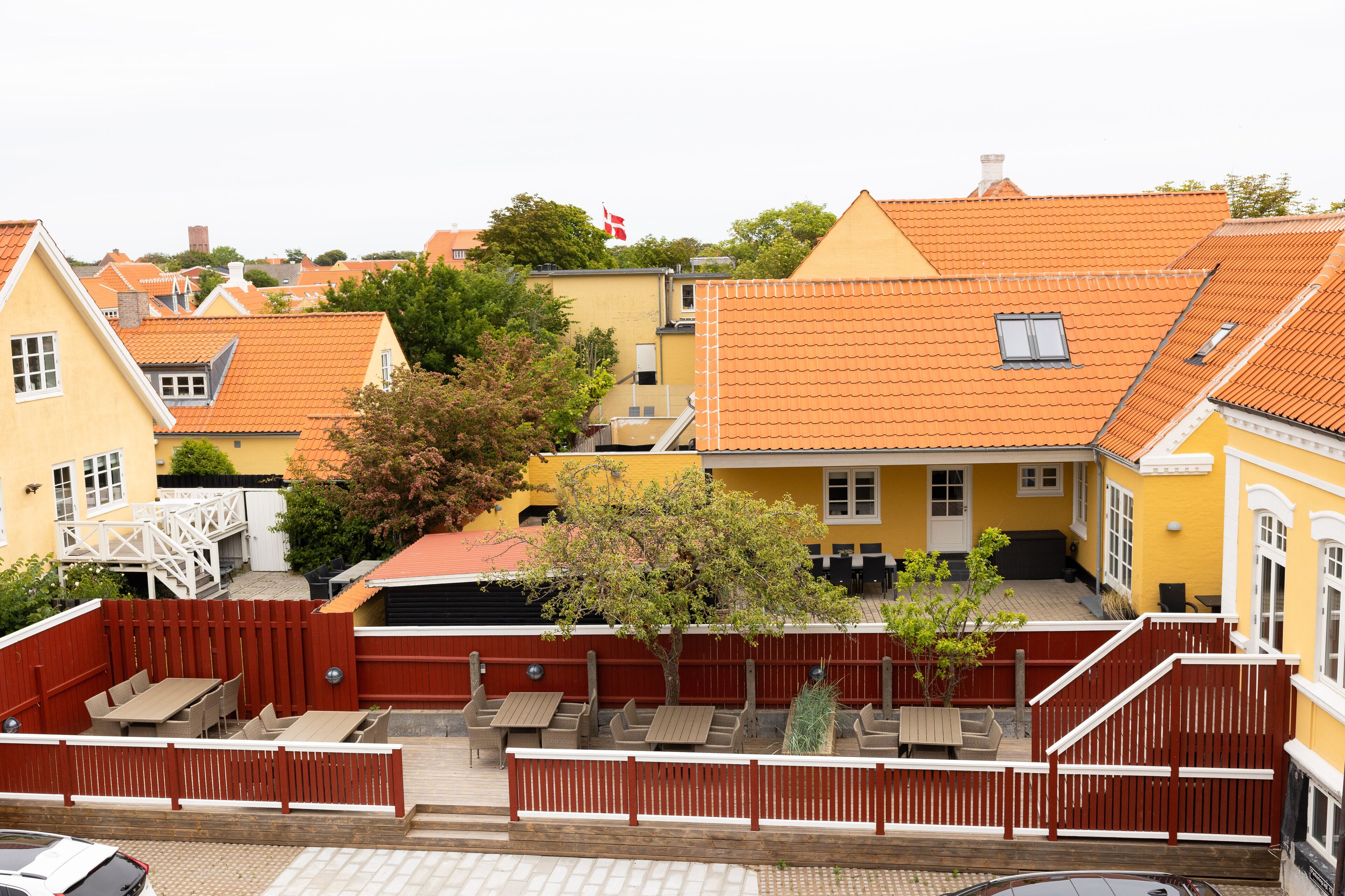 A courtyard with outdoor seating, a flag, and buildings with orange tiled roofs.
