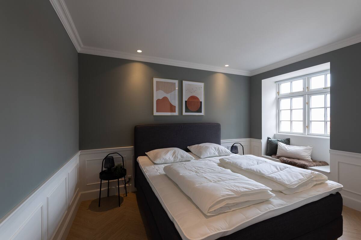 A bedroom with a large bed, a window with white shutters, and two wall-mounted artworks.