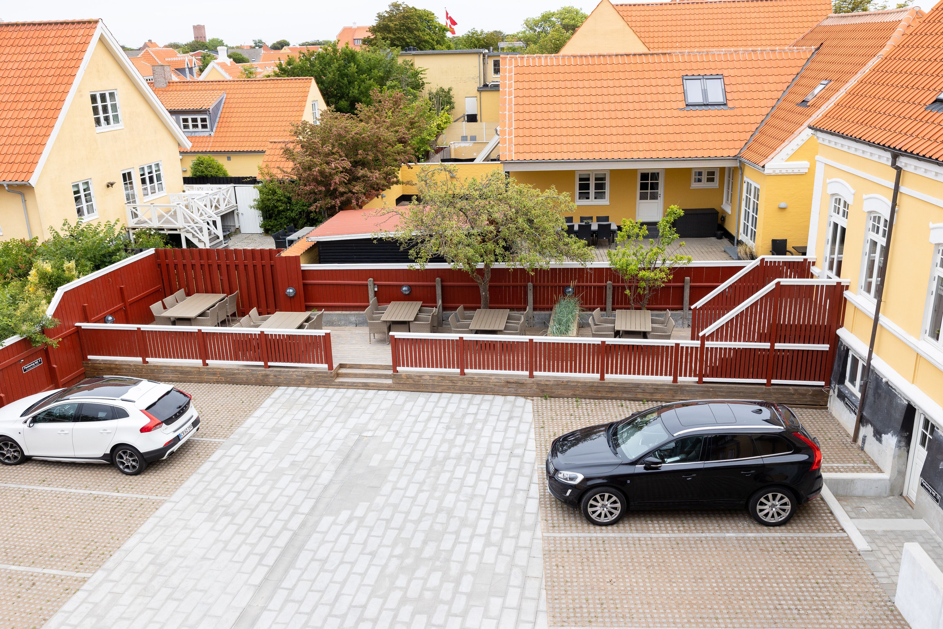 A parking area with two cars, a red fence, and a tree.