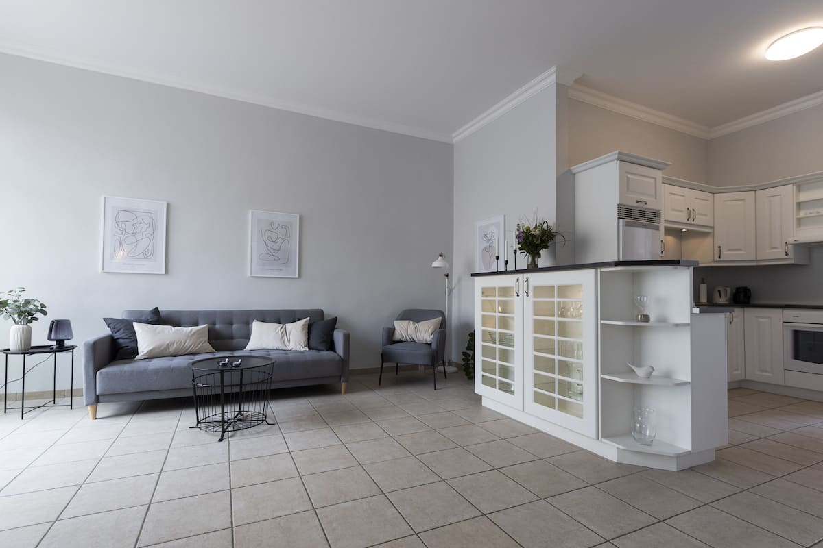 A modern living room with a grey sofa, a small round table, and a white cabinet with glass doors.