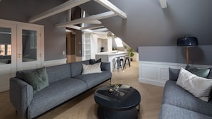 Un salon moderne avec un canapé gris, une table basse noire et une cuisine en arrière-plan.