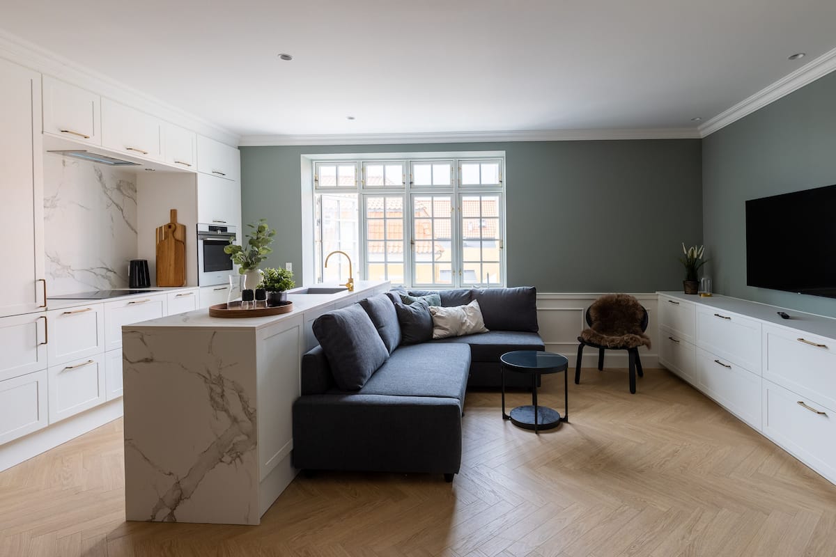 A modern kitchen with white cabinetry, a marble island, and a large window.