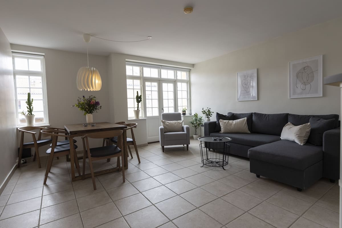A living room with a dining area, a grey sofa, a small table, and a hanging light fixture.