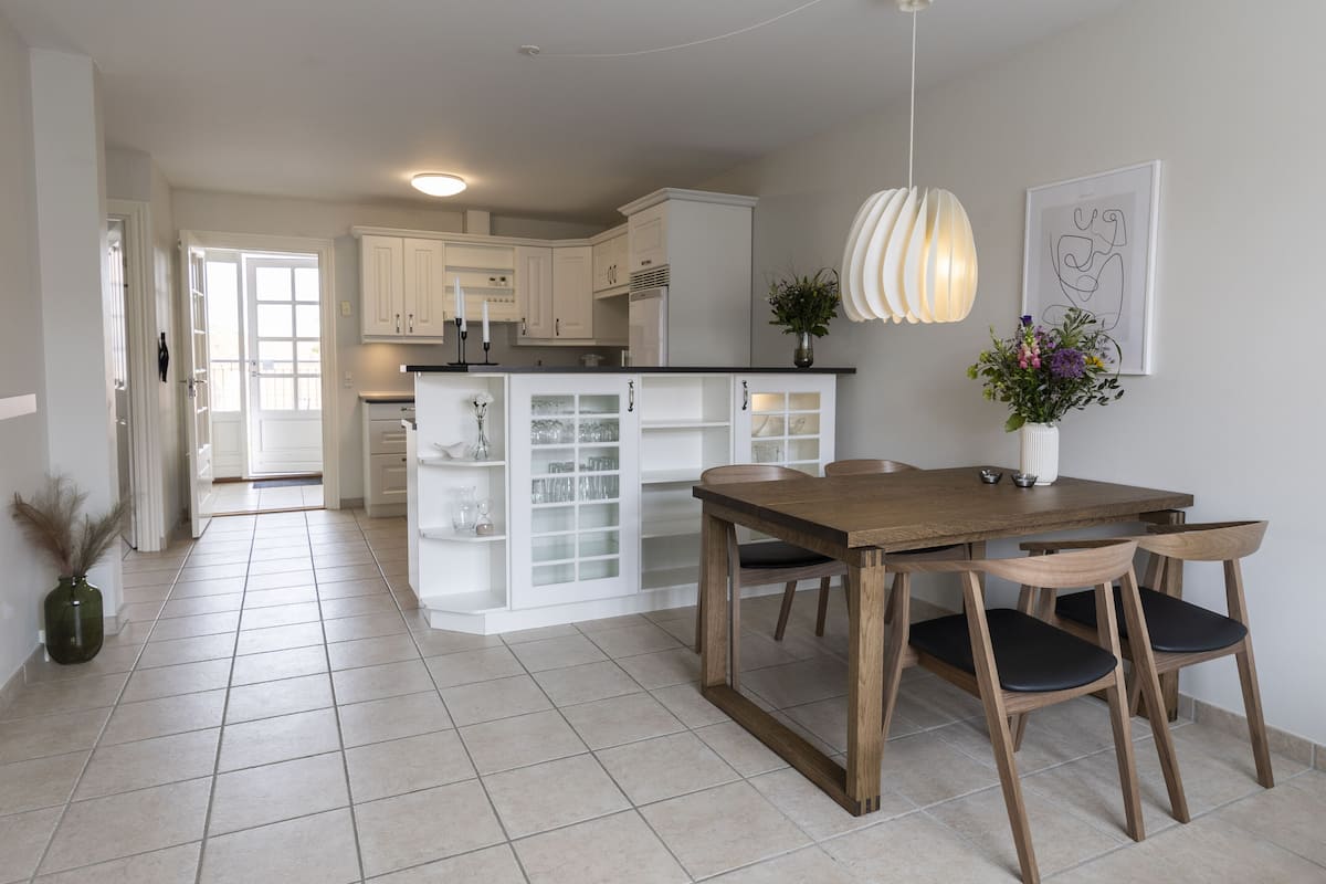 A modern kitchen with white cabinets, a wooden dining table, and a pendant light.