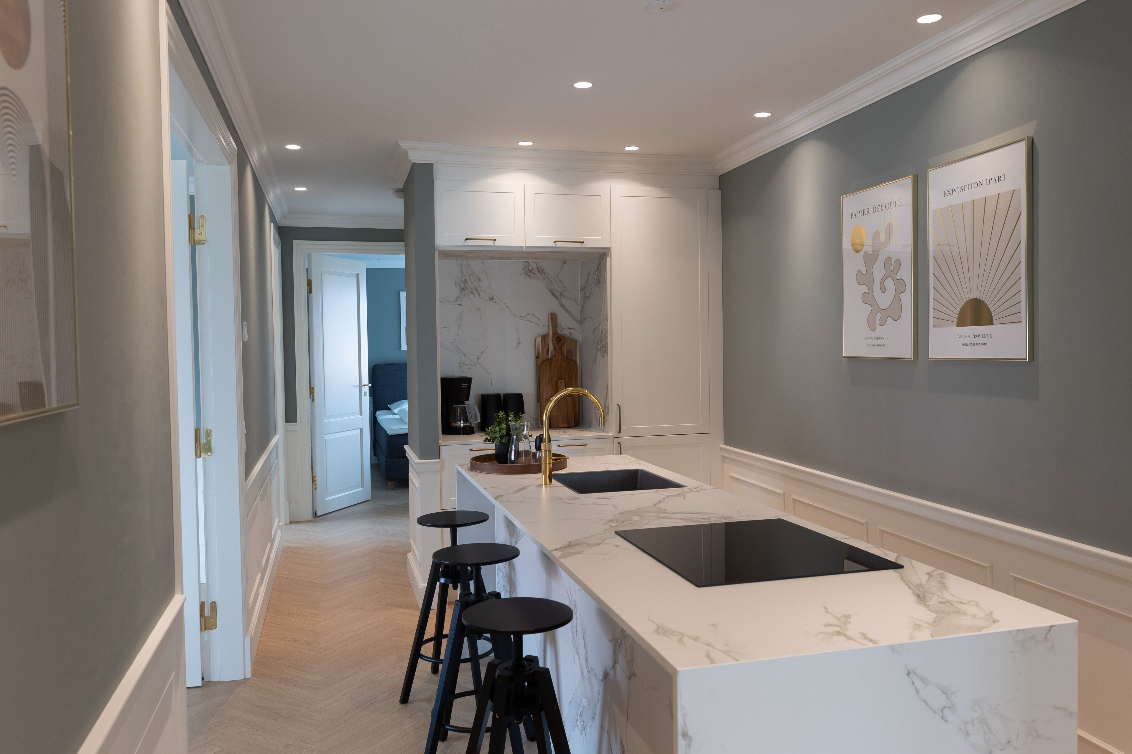 A modern kitchen with a marble countertop, black stools, and a sink.