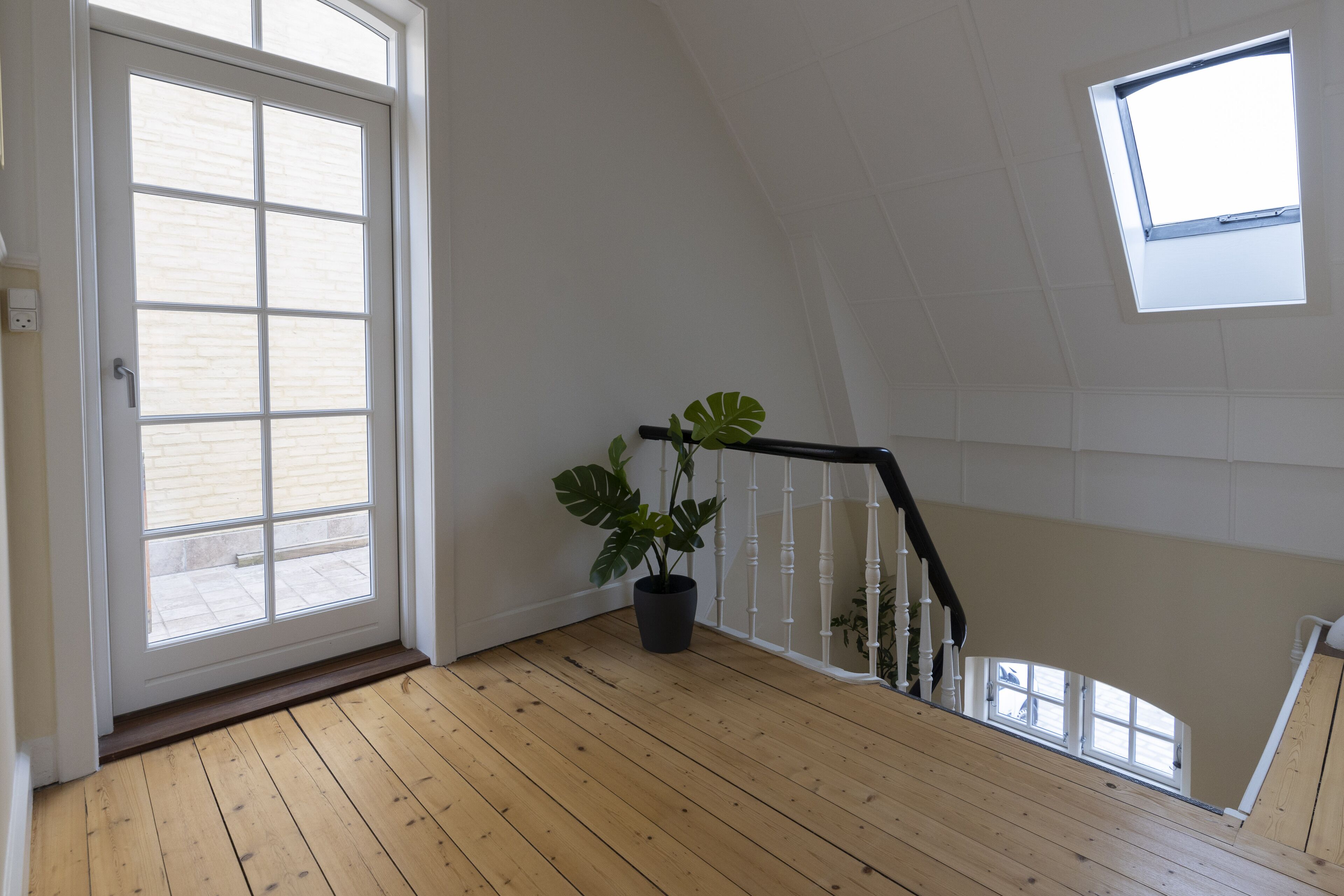 Un escalier en bois orné d’un pot de fleurs, une porte avec une fenêtre et un puits de lumière.