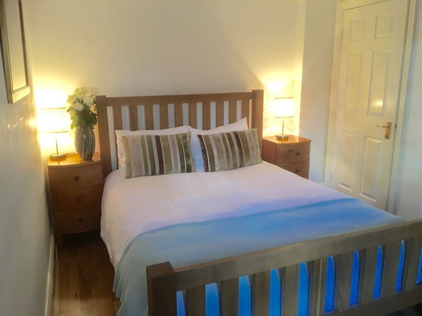 A neatly made bed with striped pillows, a wooden headboard, and two bedside tables with lamps.