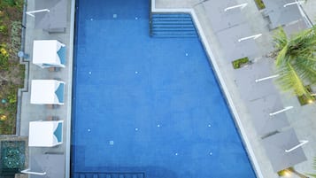 Una amplia piscina rectangular con superficie de azulejos azules, rodeada de sillas de descanso y sombrillas.