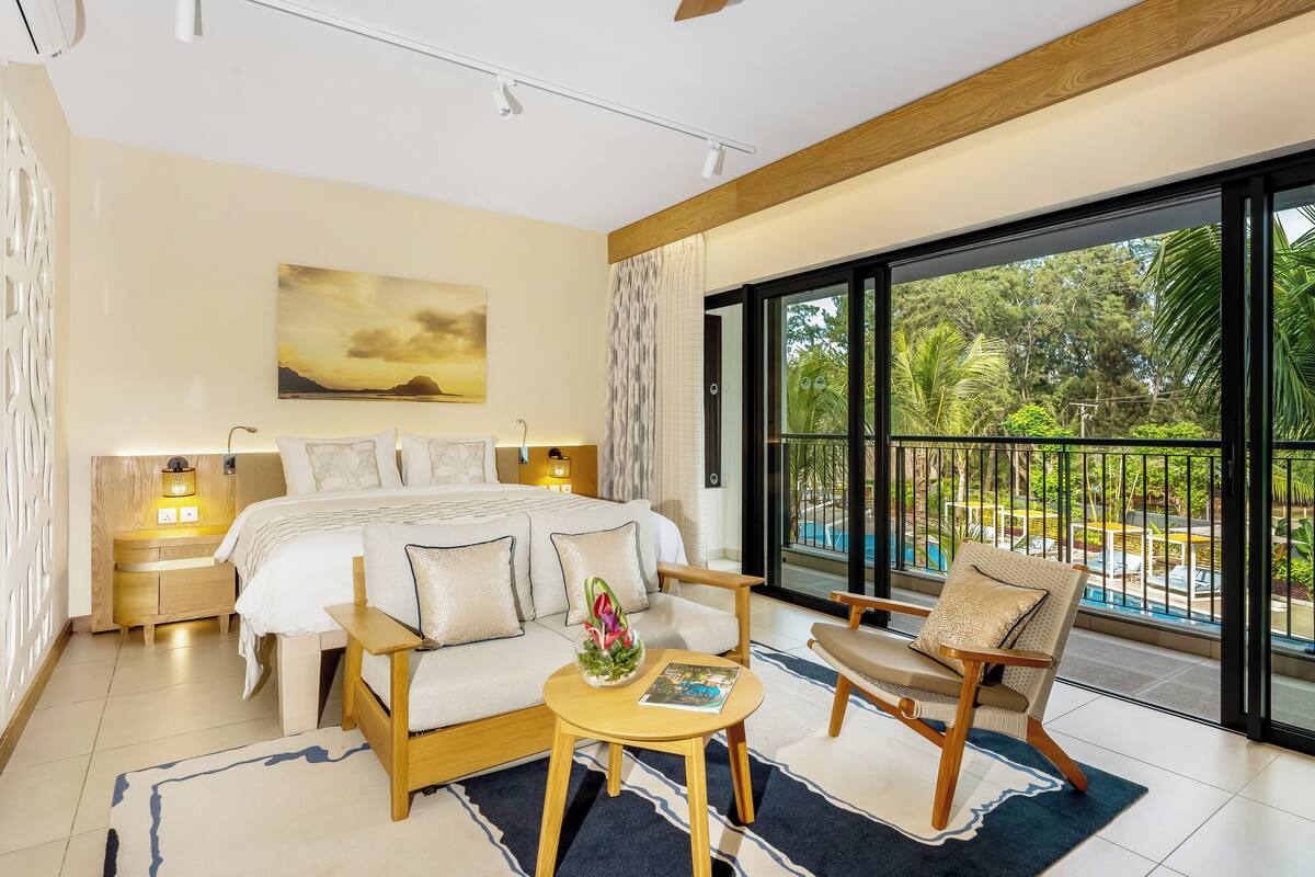 Une chambre moderne avec un grand lit, un canapé, une petite table et une vue sur une piscine et un espace verdoyant.