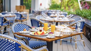 Un espace repas avec des chaises et des tables en osier, des produits pour le petit-déjeuner et une vue sur la verdure.