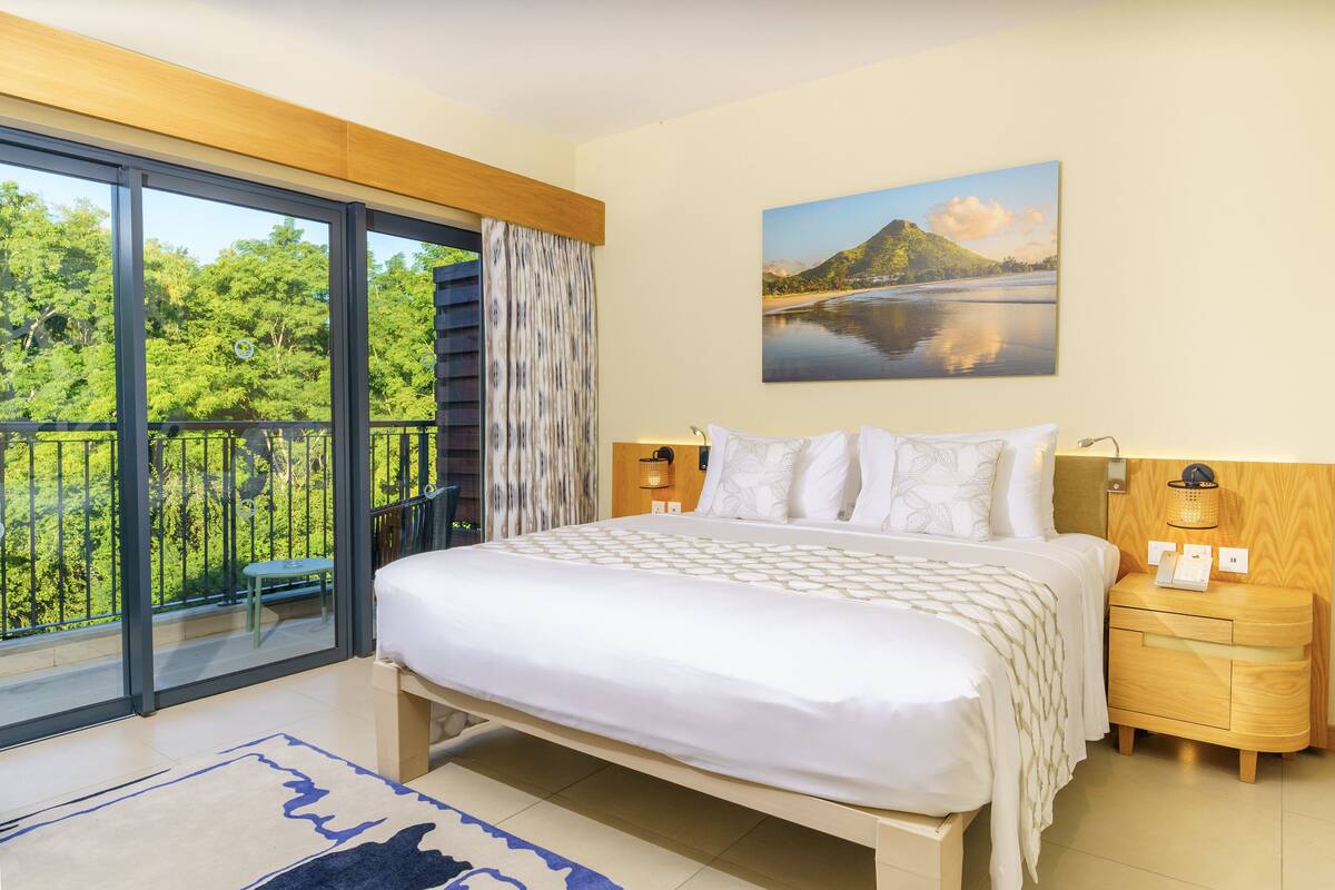 Une chambre à coucher avec un grand lit, une table de chevet, une lampe fixée au mur et un tableau représentant un paysage.