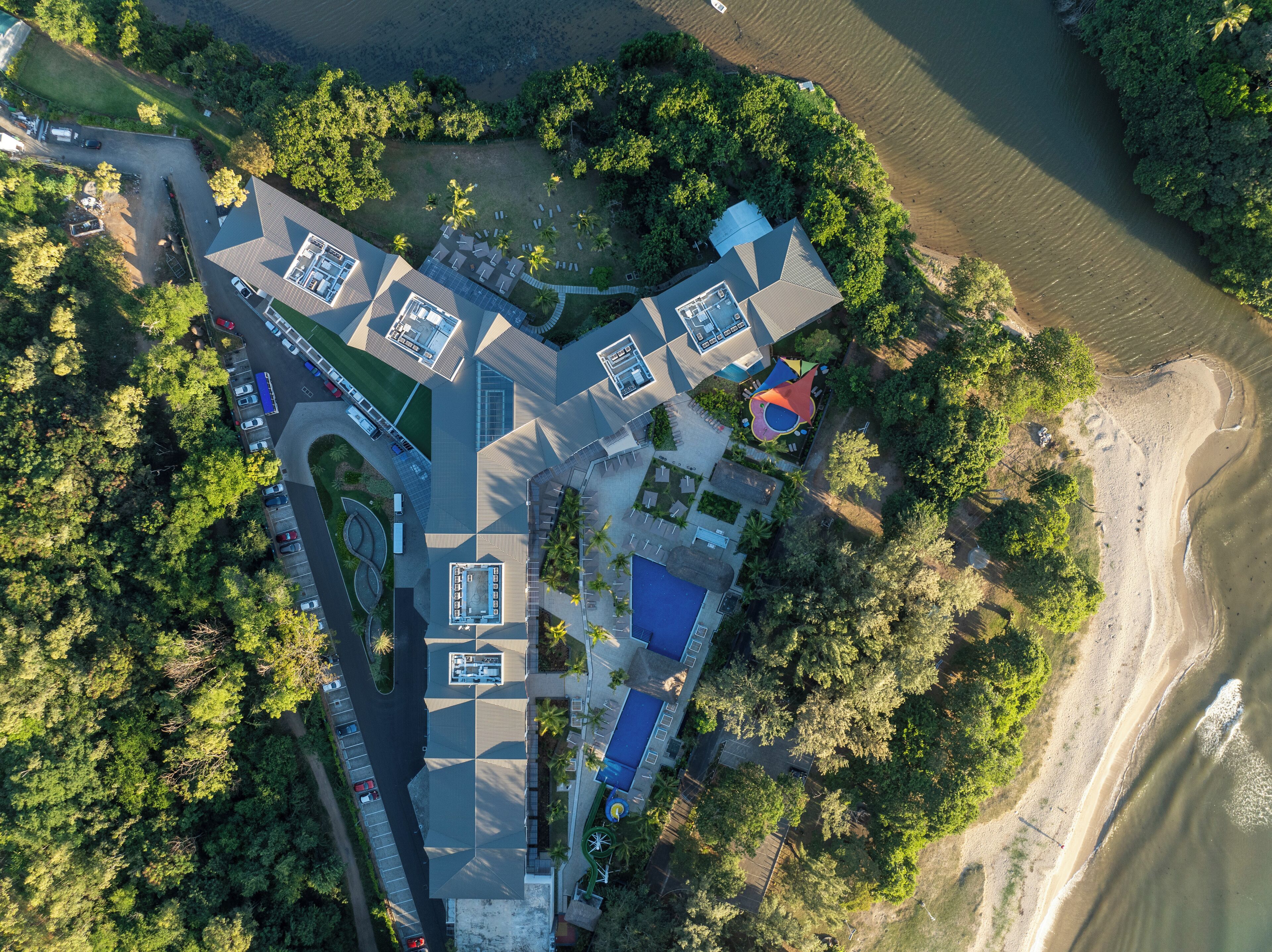 An aerial view of a resort with multiple buildings, a parking area, and a beach.