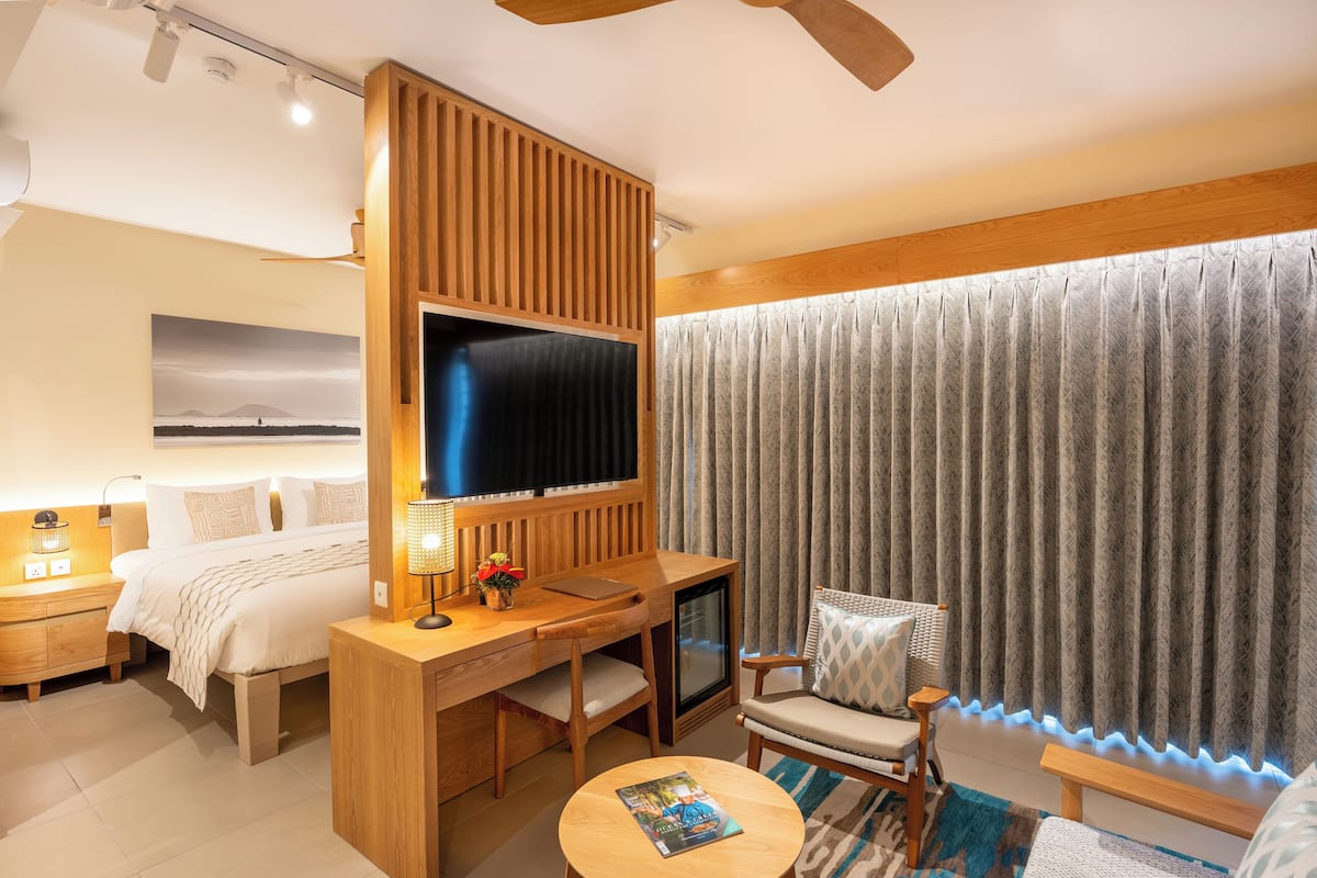 Une chambre d’hôtel moderne, dotée d’un bureau en bois, d’une télévision, d’un fauteuil confortable et d’une grande fenêtre avec des rideaux.