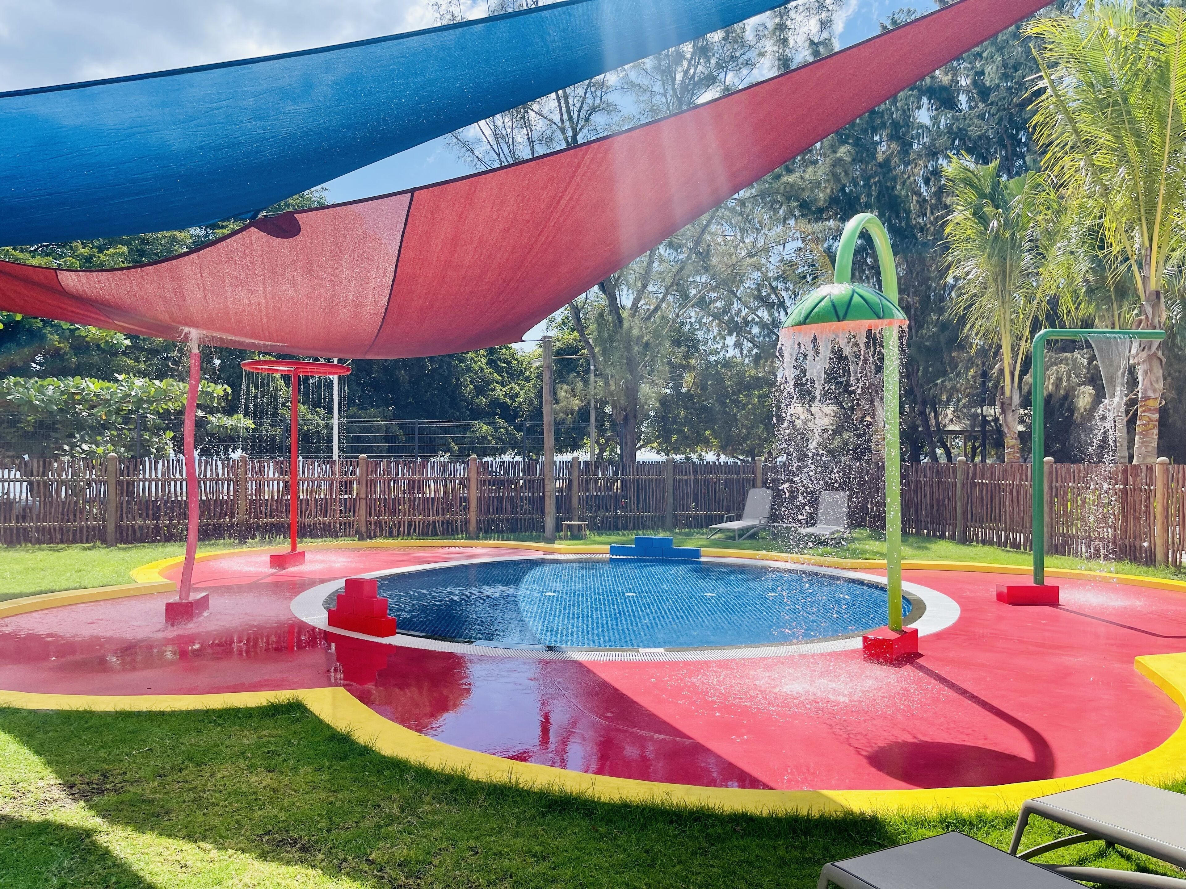 A playground with a pool, slides, and a shaded area.