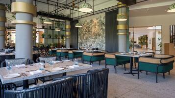 A restaurant with tables set for dining, green cushioned chairs, and hanging pendant lights.
