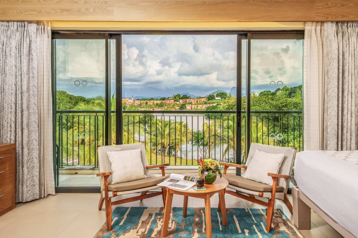 Une chambre d’hôtel dotée d’un grand balcon, de deux fauteuils en osier, d’une petite table ronde et d’un lit.