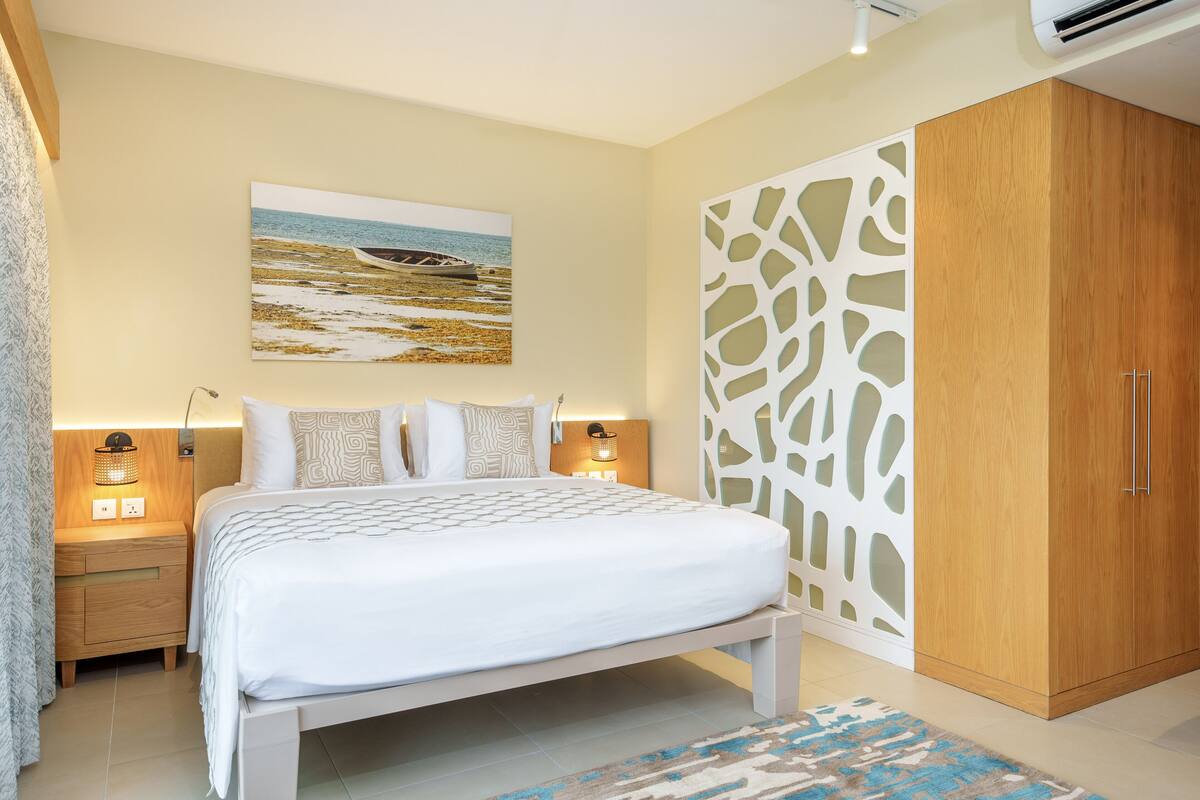 Une chambre à coucher comprenant un lit, des tables de chevet, un tableau accroché au mur, une armoire et un tapis à motifs.